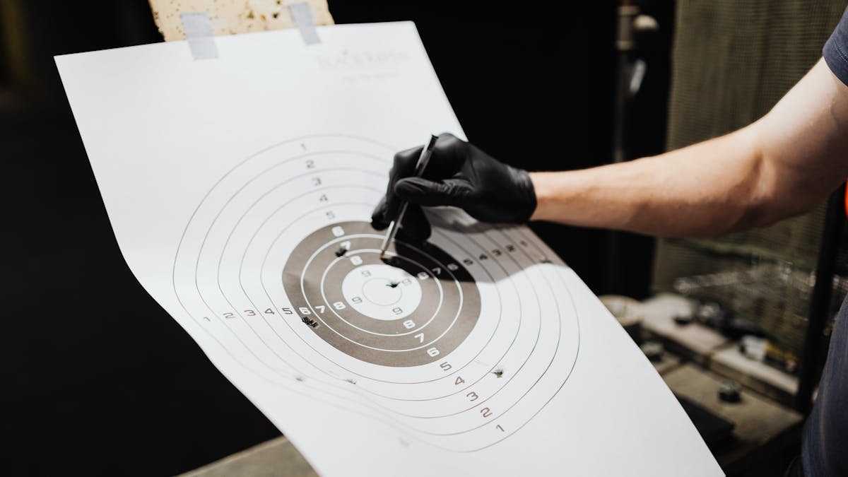 Close-up of a person marking hits on a shooting range target with a marker.